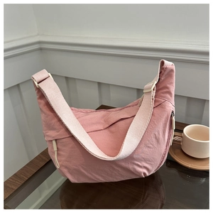 Pink crescent nylon crossbody bag on a table with a coffee cup in a cozy setting