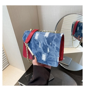 Detail of red leather crossbody bag with blue denim flap and gold chain strap in a mirror