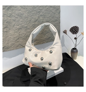 Détail du sac lune en cuir blanc crème avec clous argentés sur un décor minimaliste chic