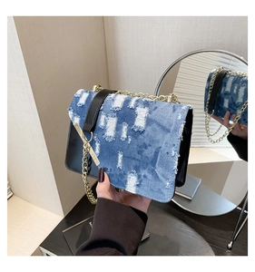 Detail of denim crossbody bag with distressed texture and gold chain strap in hand