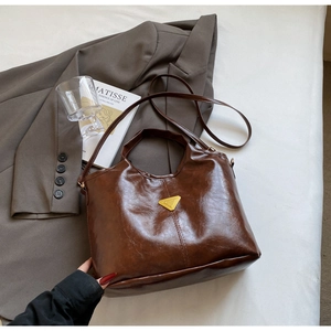 Detail of dark brown oil wax leather bucket bag with gold triangle plaque and soft texture