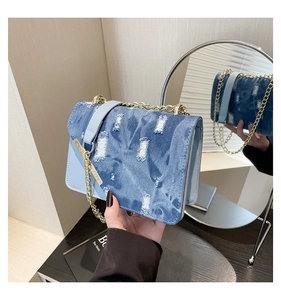 Detail of light blue denim crossbody bag with distressed texture and gold chain strap