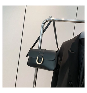 Detail of black crossbody bag with gold U-shaped buckle hanging on a metal hanger