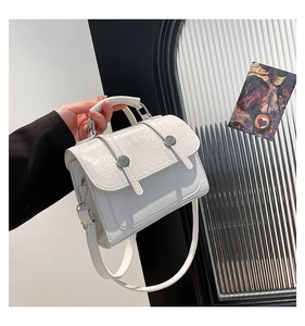 Detail view of a white crinkled patent leather crossbody bag with silver hardware accents