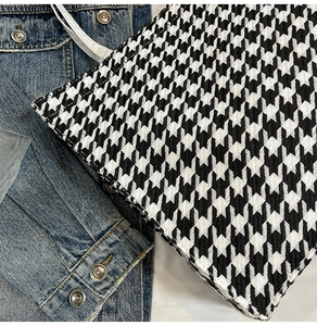 Close-up of black and white houndstooth tote bag with white handles on denim jacket
