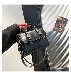 Close-up of black glossy crinkled leather shoulder bag with vintage silver buckle details
