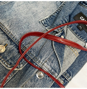 Détail d'une veste en jean avec boutons métalliques et bride en cuir verni rouge