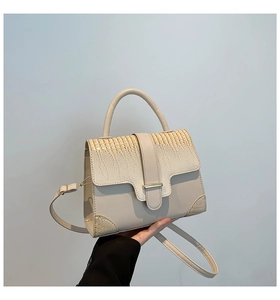 Detail of cream croc-embossed leather handbag with gold clasp and top handle texture