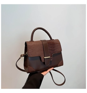 Detail of dark brown crocodile embossed leather handbag with golden metal hardware