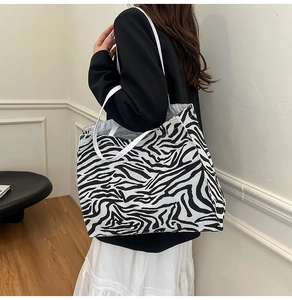 Detail of a large zebra print tote bag with white straps worn by a model in a room