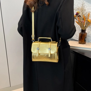 Golden metallic mini crossbody bag with glossy wrinkled texture and top handle shown on model