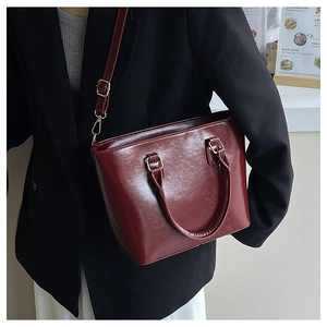 Model wearing a burgundy patent leather bucket bag with gold hardware for a chic office look