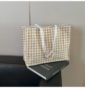Detail of woven brown houndstooth tote bag with slim white leather handles and large base