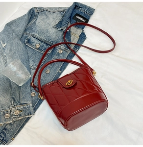 Détail d'un sac seau en cuir verni matelassé bordeaux avec un fermoir doré pivotant