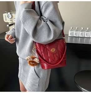 Détail d'un sac seau matelassé bordeaux avec fermoir doré et breloque peluche