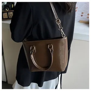 Detail of a brown glossy leather tote bag with gold hardware and adjustable strap