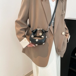 Mini black glossy saddle bag with silver studs worn cross-body on a fashion model