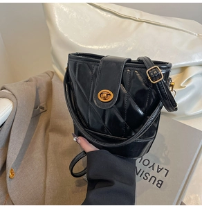 Detail view of black quilted bucket bag with gold oval twist lock and smooth leather strap