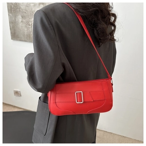 Red faux leather shoulder bag with silver buckle worn by a model in a minimalist setting