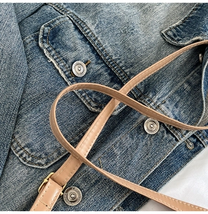Detail of light blue washed denim fabric with vintage metal button and beige leather strap