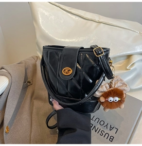 Détail d'un sac seau matelassé noir avec fermoir doré et charm de monstre en peluche