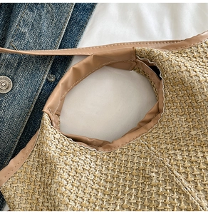 Close-up of woven straw texture and brown leather handle stitching on a beach tote bag