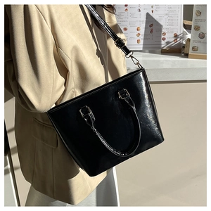 Model wearing a black glossy patent leather bucket bag with a stylish beige suit jacket