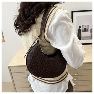 Detail of dark brown crescent bag featuring woven texture and adjustable shoulder strap