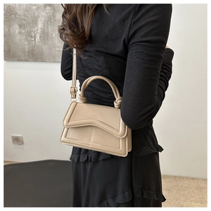 Detail of beige textured leather handbag featuring a unique knotted top handle and slim strap