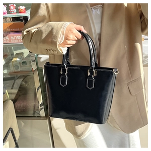 Detailed macro view of black patent leather bucket bag with gold-tone hardware accents