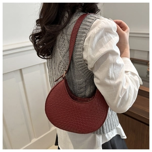 Detail of dark red crescent bag showing woven texture and adjustable shoulder strap on model