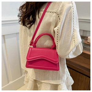 Detail of a bright pink crossbody bag showing wave-shaped flap and faux leather texture