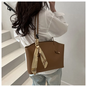 Dettaglio borsa tote in pelle marrone con cuciture bianche e sciarpa di seta annodata