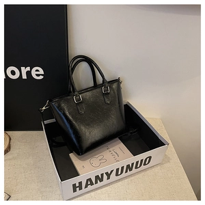 Detail of glossy black bucket bag with gold hardware in a minimalist white gift box