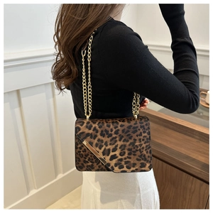 Detail of leopard print crossbody bag with gold metal trim and chain strap on a model