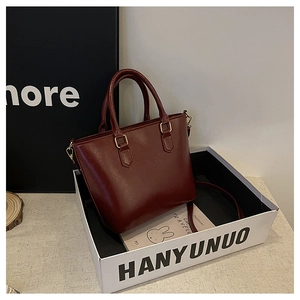Detail of burgundy leather bucket bag with gold hardware inside a white gift box