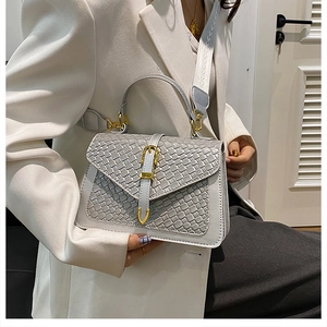Detail of light gray woven crossbody bag with golden buckle on professional suit outfit