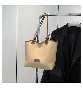 Detail of minimalist beige tote bag with brown leather FASHION tag and contrast edges