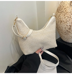Detail of cream woven shoulder bag featuring smooth leather strap and gold hardware accents