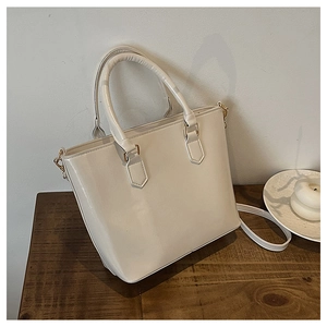 Detail of cream white faux leather bucket bag with gold metal buckles on a wooden table