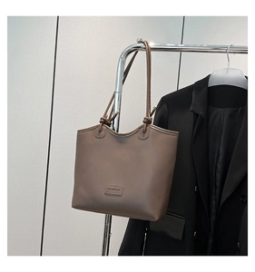 Detail of a brown faux leather tote bag with fashion label and knotted slim handles