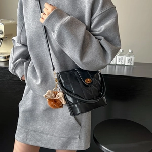 Sac seau matelassé noir avec fermoir doré et nœud en peluche porté par un mannequin