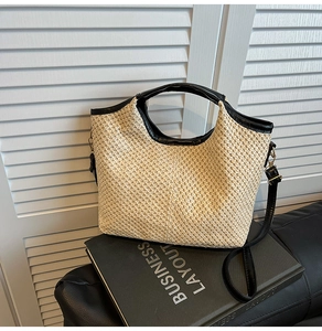 Close-up of woven straw handbag with black leather trim and detachable shoulder strap