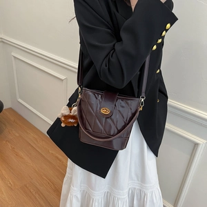 Deep brown quilted bucket bag with gold clasp and plush charm on a model
