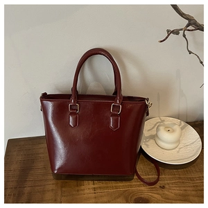 Detail of dark red glossy PU leather bucket bag with vintage gold hardware and strap