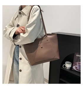 Detail of taupe leather tote bag featuring a snap-button front pocket and slim shoulder straps