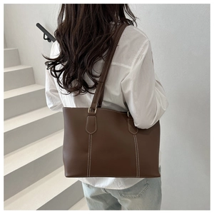 Dark brown faux leather tote bag with white contrast stitching shown on shoulder