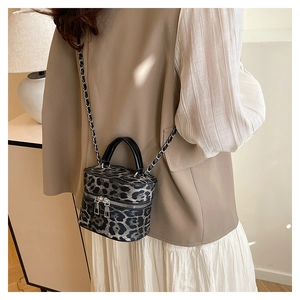 Detail of leopard print cylinder bag with silver chain and leather handle shown with model
