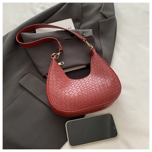 Detalle de bolso medialuna rojo con diseño de cocodrilo y hebilla dorada sobre un blazer