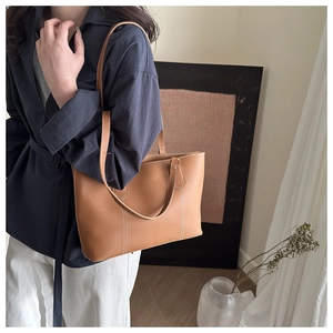 Detail of caramel faux leather tote bag featuring contrast white stitching and dual straps